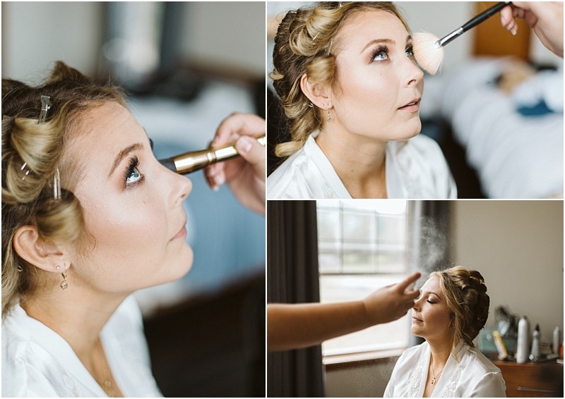 Premier snohomish & seattle wedding photographer | gsquared weddings photography a woman with curled hair in rollers gets her makeup done for her snohomish wedding She sits in a white robe while a makeup artist applies mascara blush and setting spray in a softly lit room | serving snohomish seattle                   & beyond