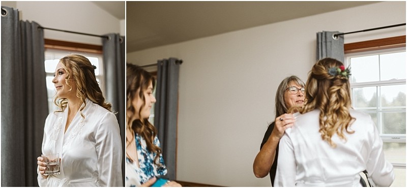 Premier snohomish & seattle wedding photographer | gsquared weddings photography a woman in a white robe holding a glass smiles while another woman adjusts something near her neckline in a softly lit room with gray curtains and a windowcapturing a serene moment before a snohomish seattle wedding | serving snohomish seattle                   & beyond