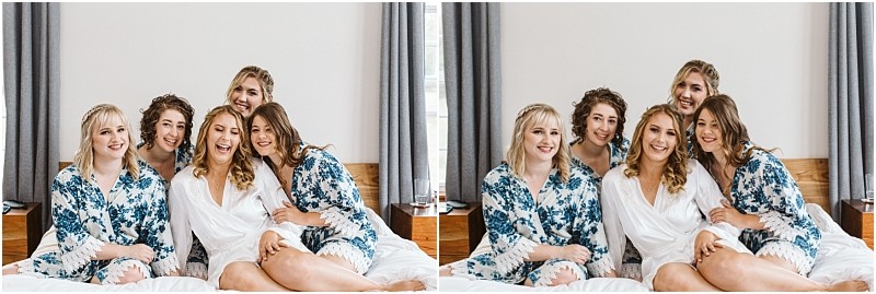Premier snohomish & seattle wedding photographer | gsquared weddings photography five women sit closely together on a bed smiling and laughing in matching floral robesexcept one in whitehinting at a snohomish wedding bridal party getting ready The bright background features curtains and a wooden headboard | serving snohomish seattle                   & beyond