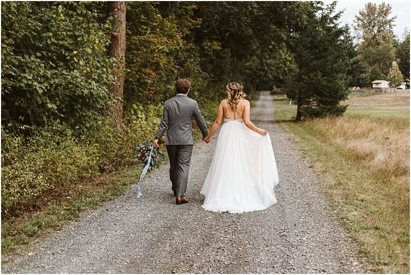Premier snohomish & seattle wedding photographer | gsquared weddings photography a bride in a white gown and a groom in a gray suit walk hand in hand down a gravel path surrounded by greenery at their snohomish wedding with trees and grass lining both sides | serving snohomish seattle                   & beyond
