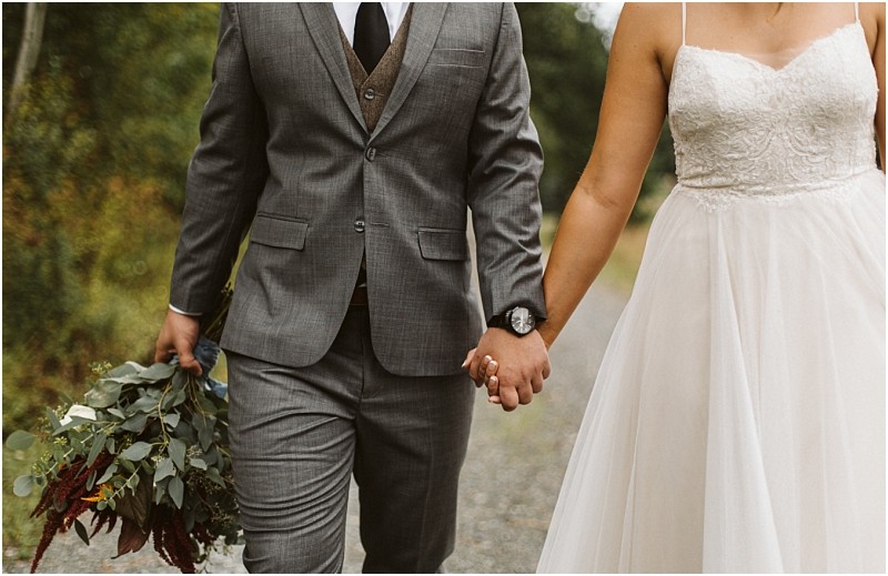 Premier snohomish & seattle wedding photographer | gsquared weddings photography a couple dressed in wedding attire holds hands while walking outdoors at a snohomish seattle wedding The person on the left wears a gray suit and holds a bouquet the person on the right wears a white lace wedding dress | serving snohomish seattle                   & beyond