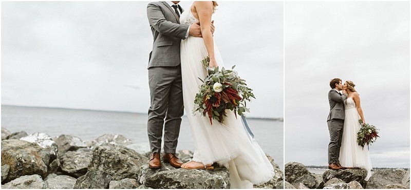 Premier snohomish & seattle wedding photographer | gsquared weddings photography a bride and groom share an intimate moment on a rocky shore near the water The bride holds a bouquet of greenery and burgundy flowers while the groom wears a gray suitcapturing a romantic snohomish seattle wedding scene beneath a cloudy sky | serving snohomish seattle                   & beyond