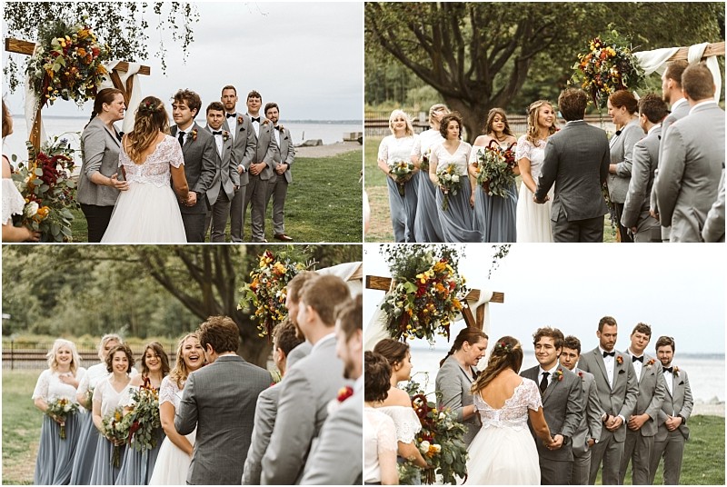 Premier snohomish & seattle wedding photographer | gsquared weddings photography a bride and groom stand together at a snohomish outdoor wedding ceremony by the water surrounded by bridesmaids in blue dresses and groomsmen in gray suits under a floral arch Everyone looks joyful and engaged | serving snohomish seattle                   & beyond