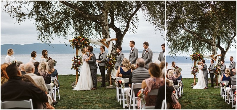 Premier snohomish & seattle wedding photographer | gsquared weddings photography a couple stands under a floral arch exchanging vows at an outdoor snohomish lakeside wedding ceremony near seattle surrounded by their wedding party and guests on white chairs with trees and water in the background | serving snohomish seattle                   & beyond