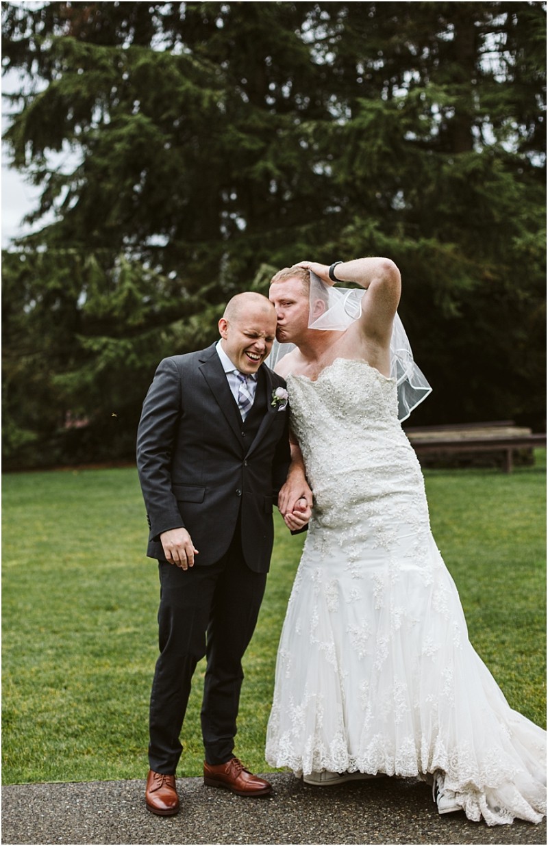 Premier snohomish & seattle wedding photographer | gsquared weddings photography two people stand outside on grass at a snohomish seattle wedding One in a dark suit laughs while holding hands with the other who wears a white wedding dress and playfully flexes an arm muscle Trees are visible in the background | serving snohomish seattle                   & beyond
