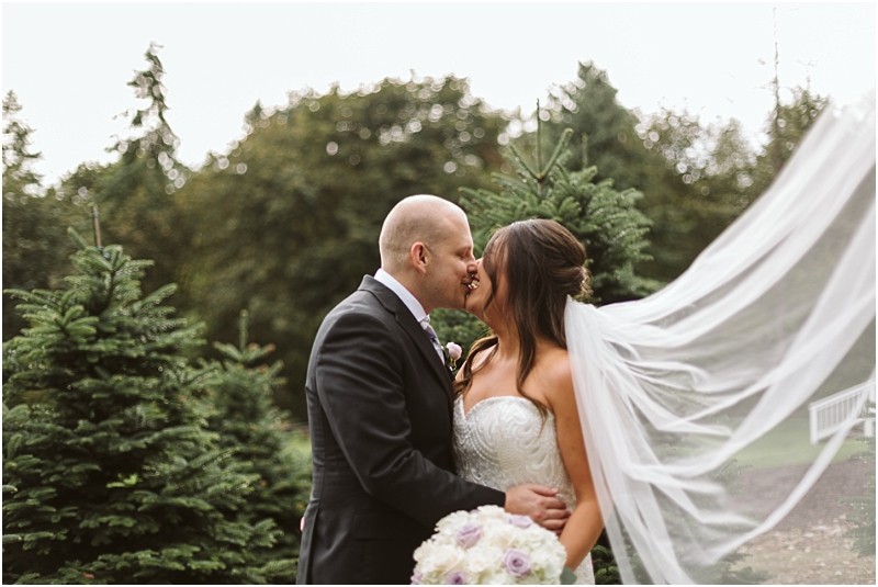 Premier snohomish & seattle wedding photographer | gsquared weddings photography a bride and groom kiss outdoors among evergreen trees at their romantic snohomish wedding The brides strapless gown and flowing veil paired with the grooms dark suit create a timeless seattle engagement moment surrounded by nature | serving snohomish seattle                   & beyond