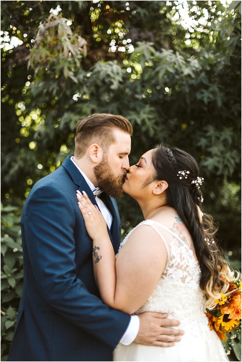 Premier snohomish & seattle wedding photographer | gsquared weddings photography a bride and groom dressed in a white lace wedding dress and navy suit lovingly kiss outdoors in front of lush green trees Capturing a magical snohomish seattle wedding moment the bride holds a bouquet and has flowers in her hair | serving snohomish seattle                   & beyond