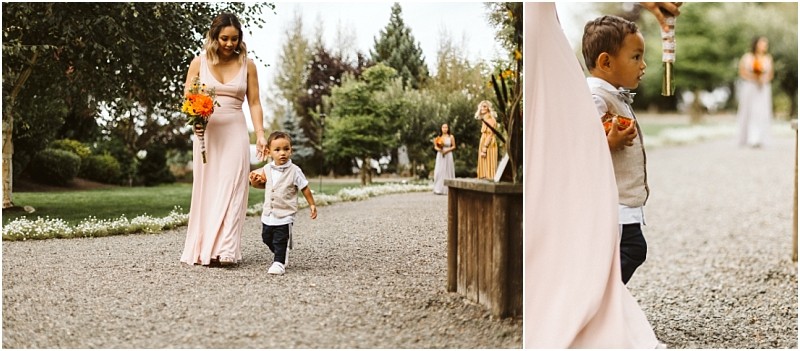 Premier snohomish & seattle wedding photographer | gsquared weddings photography a woman in a pink dress holding orange flowers walks outdoors on a gravel path with a young boy in a vest and bowtie slightly ahead of her Lush greenery and other guests set the scene for this charming snohomish seattle wedding moment | serving snohomish seattle                   & beyond