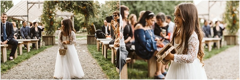 Premier snohomish & seattle wedding photographer | gsquared weddings photography a young flower girl in a white lace dress walks down an outdoor aisle at a snohomish wedding holding a wooden box while guests watch and smile during the ceremony | serving snohomish seattle                   & beyond