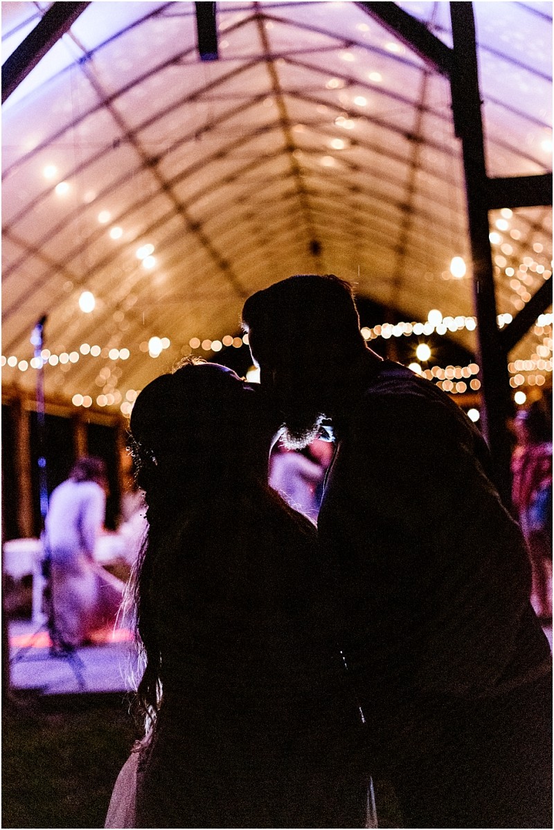Premier snohomish & seattle wedding photographer | gsquared weddings photography silhouetted couple facing each other under a transparent arched ceiling with string lights at a snohomish seattle wedding engagement surrounded by soft warm lighting and blurred people in the background creating a romantic atmosphere | serving snohomish seattle                   & beyond