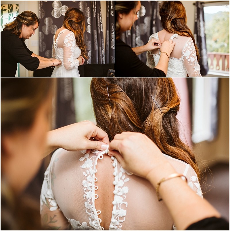 Premier snohomish & seattle wedding photographer | gsquared weddings photography a woman helps a bride in a white lace dress button up her gown The photos focus on the brides back highlighting intricate lace details and hands fastening buttonscapturing a beautiful seattle wedding moment near a window with curtains | serving snohomish seattle                   & beyond