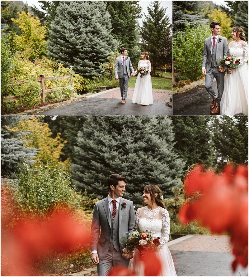Premier snohomish & seattle wedding photographer | gsquared weddings photography a bride in a white dress and groom in a gray suit walk hand in hand outdoors at a snohomish seattle wedding surrounded by greenery and autumn trees smiling at each other with red flowers in the foreground | serving snohomish seattle                   & beyond