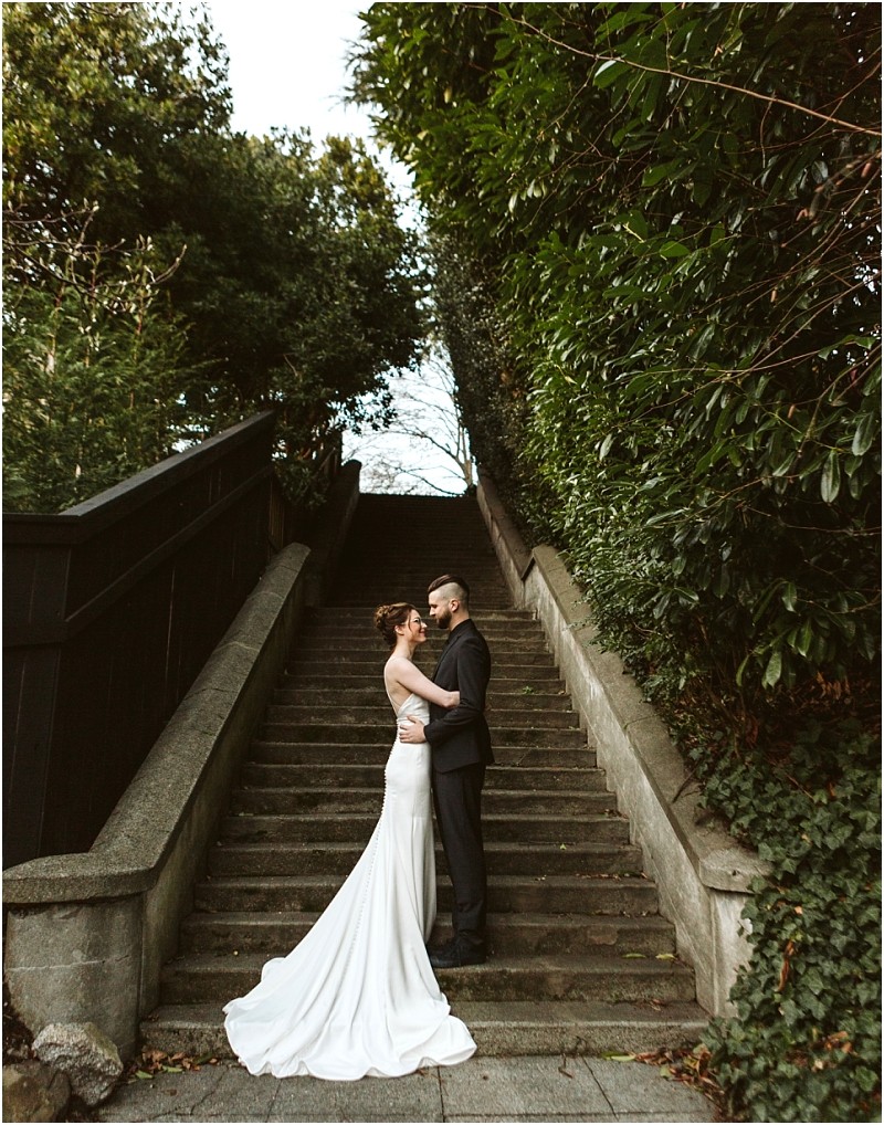 Premier snohomish & seattle wedding photographer | gsquared weddings photography a bride and groom embrace on outdoor stone steps surrounded by greenery and trees at a tranquil snohomish setting The bride in a long white dress and the groom in a dark suit gaze at each other lovingly after their seattle wedding engagement | serving snohomish seattle                   & beyond