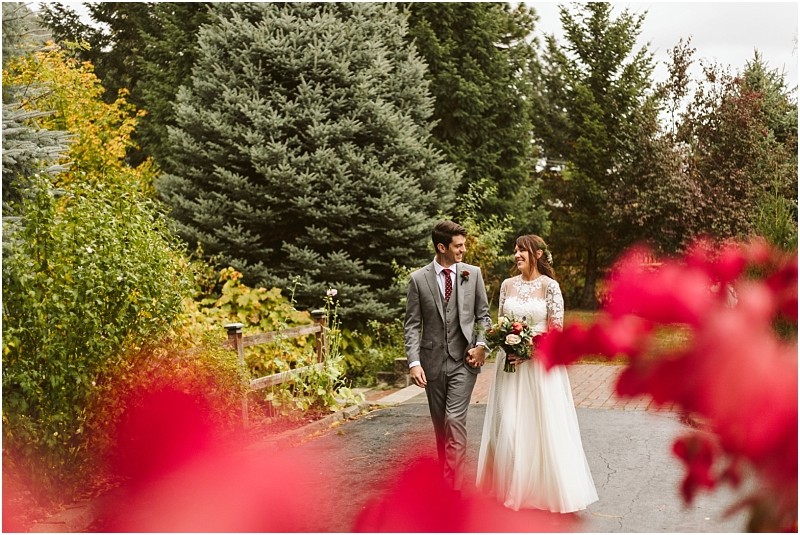 Premier snohomish & seattle wedding photographer | gsquared weddings photography a bride and groom walk hand in hand down a garden path smiling at each other surrounded by lush greenery and vibrant red flowerscapturing the romance of a snohomish seattle wedding engagement | serving snohomish seattle                   & beyond