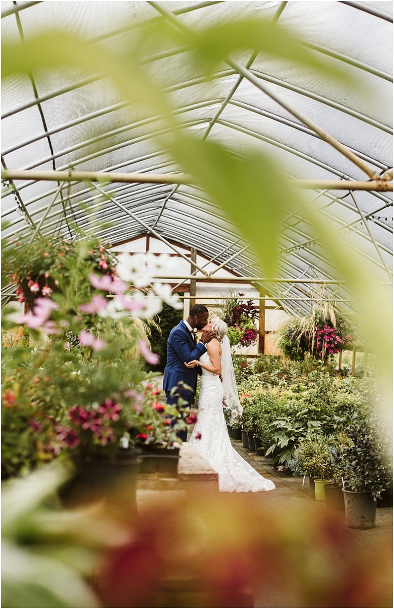 Premier snohomish & seattle wedding photographer | gsquared weddings photography a bride and groom share a kiss in a greenhouse full of flowers and greenery framed by leaves and hanging plants under a curved translucent roof during their romantic snohomish seattle wedding | serving snohomish seattle                   & beyond