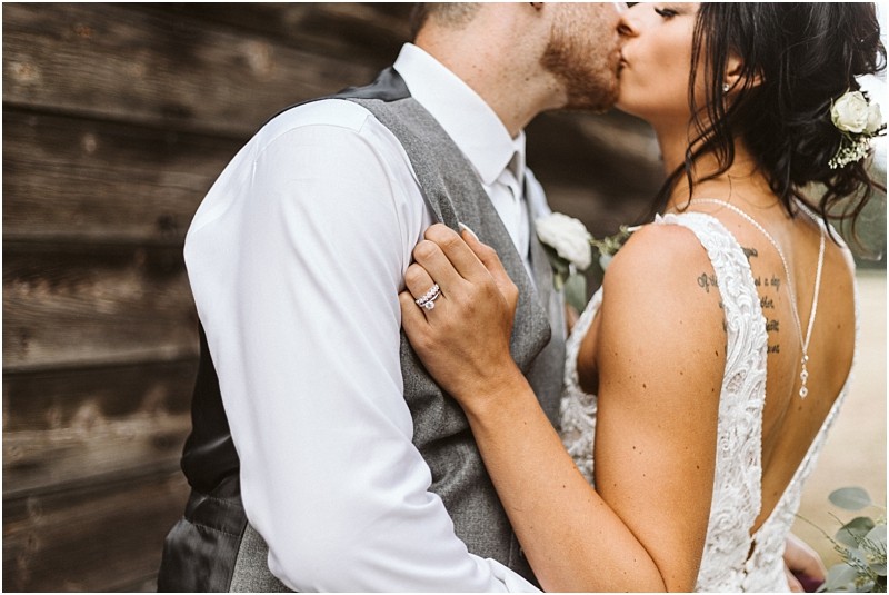 Snohomish & seattle wedding photographer | gsquared weddings photography a bride and groom share a kiss outdoors near a rustic wooden wall Showcasing her wedding ring and back tattoo the bride in lace embraces her grooman unforgettable moment among the best of 2019 wedding couples | wedding photo by gsquared weddings