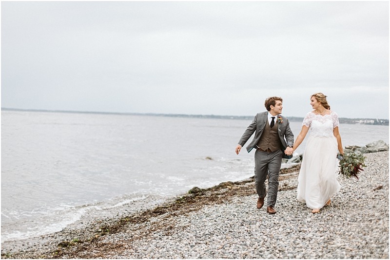 Snohomish & seattle wedding photographer | gsquared weddings photography a bride and groom walk hand in hand along a rocky beach dressed in wedding attire with the ocean and cloudy sky in the backgrounda stunning moment among the best of 2019 for wedding couples | wedding photo by gsquared weddings