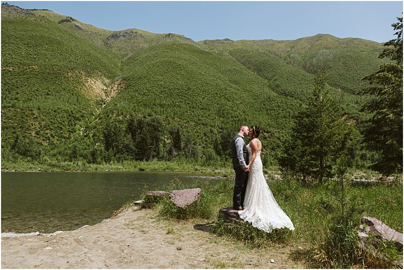 Snohomish & seattle wedding photographer | gsquared weddings photography a bride and groom stand holding hands and kissing by a lake surrounded by lush green mountains and trees under a clear skya stunning moment among our best of 2019 wedding couples | wedding photo by gsquared weddings