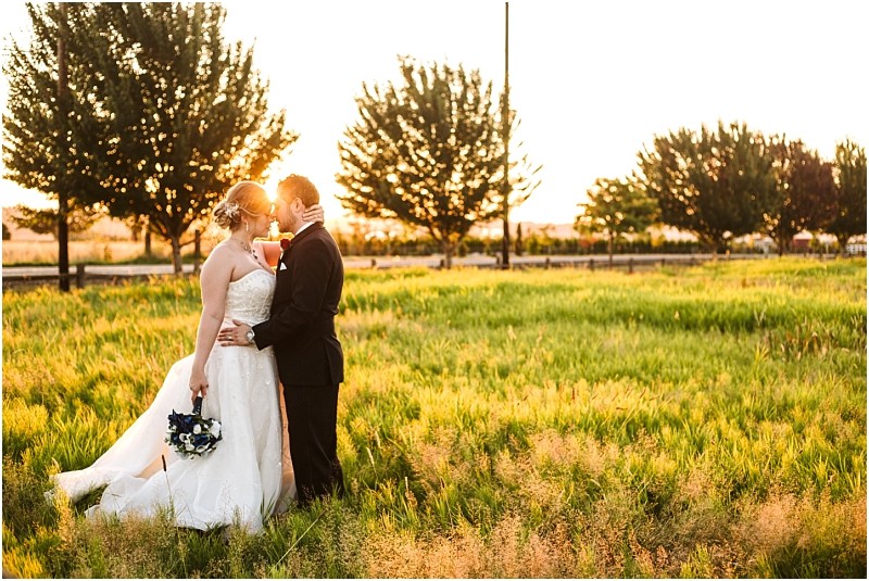 Snohomish & seattle wedding photographer | gsquared weddings photography a bride and groom honored among the best of 2019 wedding couples stand in a sunlit grassy field at sunset gazing into each others eyes The bride holds a bouquet in her white dress beside the groom in a black suit with trees and a road behind them | wedding photo by gsquared weddings