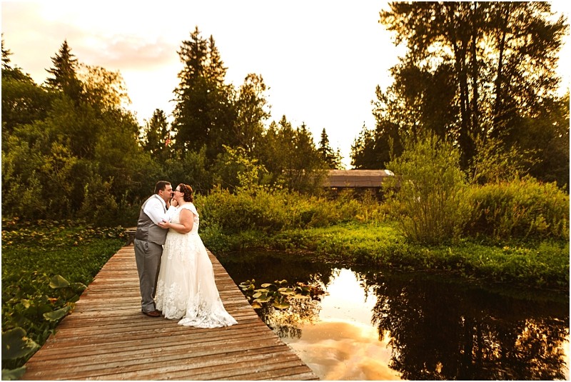 Snohomish & seattle wedding photographer | gsquared weddings photography a bride and groom one of the top wedding couples and best of 2019 stand close together on a wooden dock over a pond surrounded by lush greenery and reflecting water beneath a golden sunset sky | wedding photo by gsquared weddings