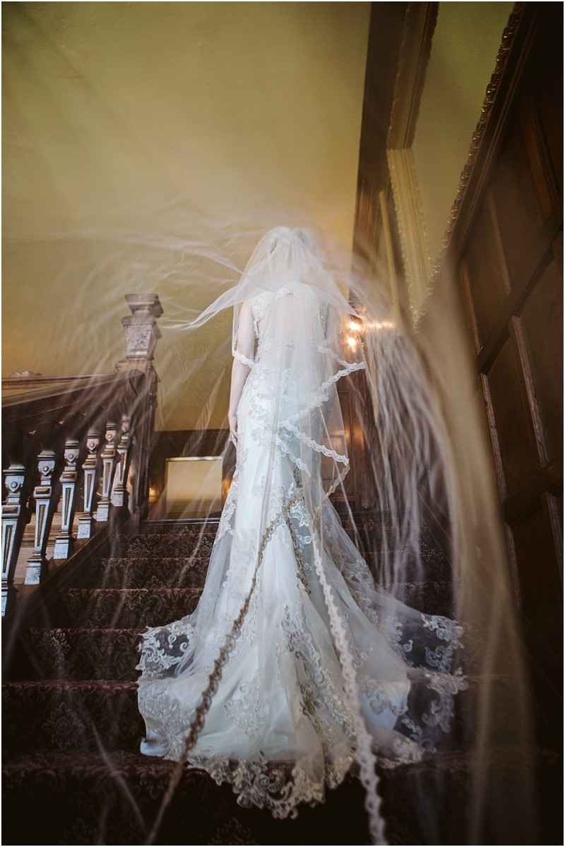 Snohomish & seattle wedding photographer | gsquared weddings photography a bride in a white lace wedding dress stands on a carpeted staircase her long flowing veil trailing behind her and creating a dreamy ethereal effect This softly lit elegant scene captures the magic of wedding couples at their best of 2019 | wedding photo by gsquared weddings
