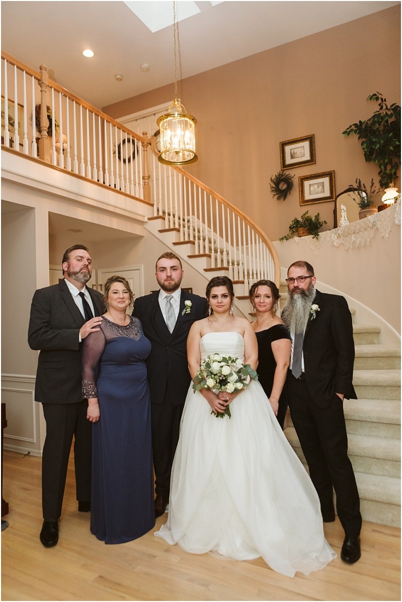 Snohomish & seattle wedding photographer | gsquared weddings photography a bride in a white gown holding a bouquet stands with her groom and four adults all dressed formally posing together on the staircase of a warmly lit home during their marysville wedding | wedding photo by gsquared weddings