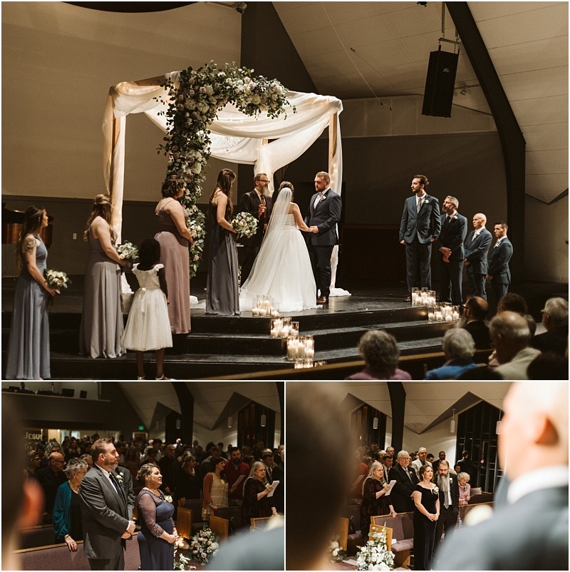 Snohomish & seattle wedding photographer | gsquared weddings photography a beautiful marysville wedding ceremony takes place indoors with a bride and groom standing under a floral arch Bridesmaids and groomsmen are by their side as guests watch surrounded by candles decorating the stage | wedding photo by gsquared weddings