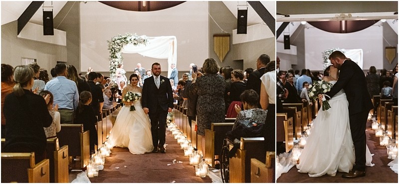 Snohomish & seattle wedding photographer | gsquared weddings photography a bride and groom walk down a candle lit aisle in a church during their marysville wedding as guests stand and applaud on the right they share a kiss at the end of the aisle holding bouquets and dressed in wedding attire | wedding photo by gsquared weddings