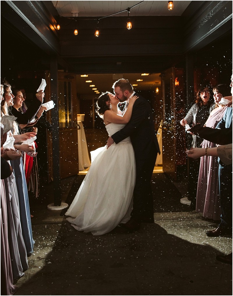 Snohomish & seattle wedding photographer | gsquared weddings photography a bride and groom share a kiss under string lights at their marysville wedding while guests in formal attire celebrate tossing confetti around them at night | wedding photo by gsquared weddings