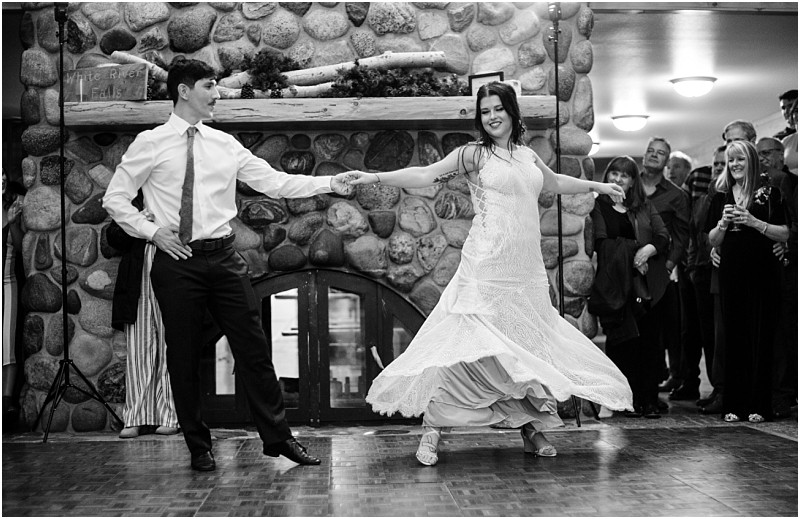 Snohomish & seattle wedding photographer | gsquared weddings photography a couple dances together in front of a stone fireplace at a leavenworth wedding the womans dress twirling as she spins An audience looks on and smiles some holding drinks in a warmly lit room | wedding photo by gsquared weddings