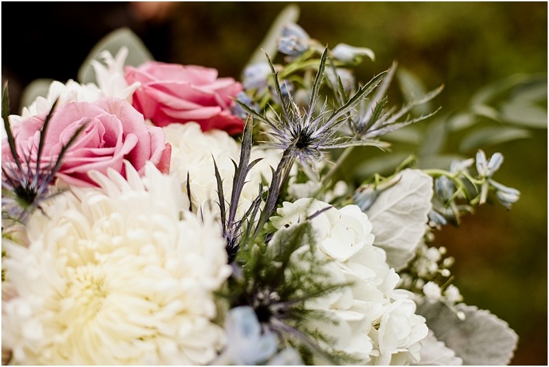 Snohomish & seattle wedding photographer | gsquared weddings photography a close up of a bouquet featuring pink roses white chrysanthemums light blue thistles and assorted greenery set against a blurred natural backgroundperfect for a love with a view or machias elopement | wedding photo by gsquared weddings