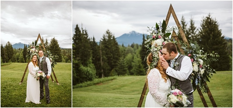 Snohomish & seattle wedding photographer | gsquared weddings photography a bride and groom stand smiling outdoors in front of a large triangular wooden arch decorated with flowers In a close up the groom kisses the bridepure love with a viewamid mountains pine trees and cloudy skies at their machias elopement | wedding photo by gsquared weddings