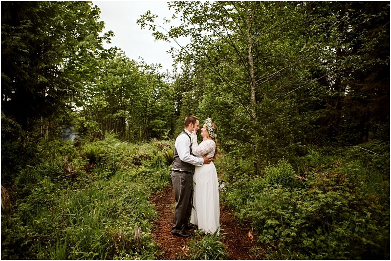 Snohomish & seattle wedding photographer | gsquared weddings photography a bride and groom share an intimate moment on a forest path surrounded by lush green treescapturing the essence of love with a view during their machias elopement | wedding photo by gsquared weddings