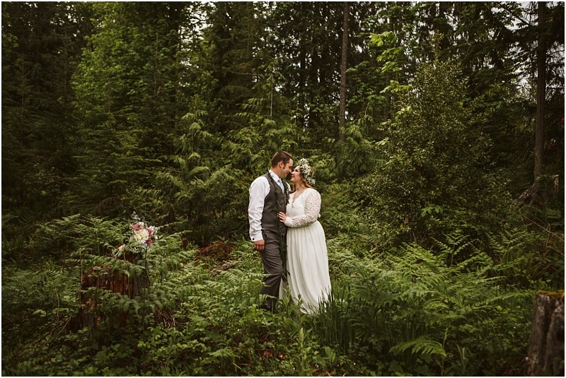 Snohomish & seattle wedding photographer | gsquared weddings photography a bride and groom share an intimate embrace in a lush green forest radiating happiness The brides flower crown and the grooms vest add charm to this machias elopement capturing true love with a view in a stunning natural setting | wedding photo by gsquared weddings