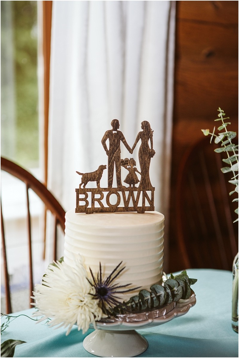 Snohomish & seattle wedding photographer | gsquared weddings photography a white frosted cake with a wooden topper showing a family child and dog with brown beneath them Decorated with white and purple flowers and greenery this machias elopement treat is a true symbol of love with a view on a white stand | wedding photo by gsquared weddings