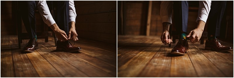 Snohomish & seattle wedding photographer | gsquared weddings photography a person in dress pants and a white shirt bends down to tie the laces of brown leather shoes on a wooden floor preparing quietly for their marionfield farm elopement in a dimly lit room | wedding photo by gsquared weddings
