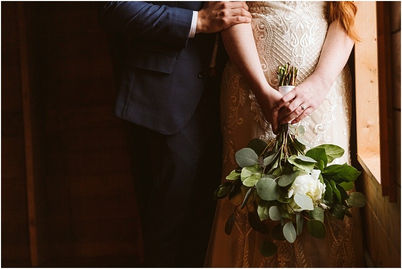 Snohomish & seattle wedding photographer | gsquared weddings photography a bride holding a bouquet of white flowers and greenery stands next to a groom in a dark suit at their marionfield farm elopement both partially illuminated by natural light from a window | wedding photo by gsquared weddings