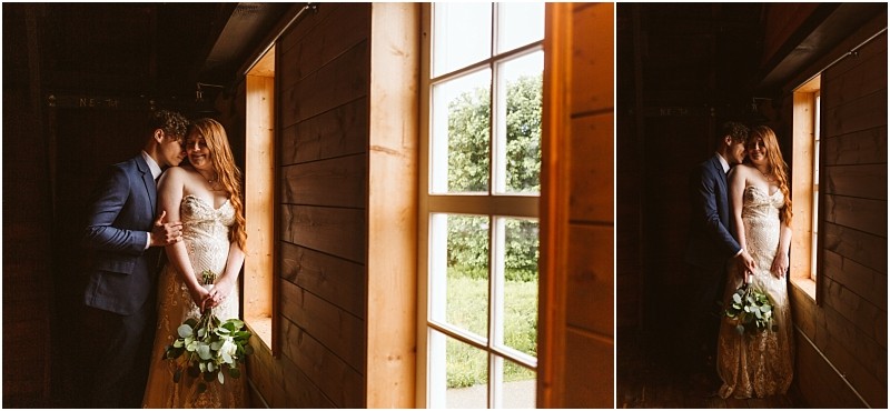 Snohomish & seattle wedding photographer | gsquared weddings photography a couple stands close together by a wooden window at their marionfield farm elopement the groom in a blue suit and the bride in a strapless dress holding a bouquet soft daylight streaming in creating a warm and intimate atmosphere | wedding photo by gsquared weddings