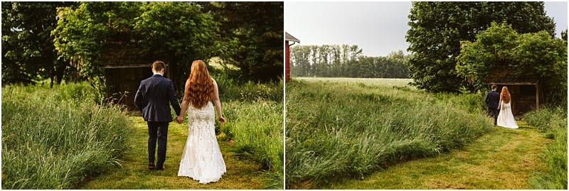 Snohomish & seattle wedding photographer | gsquared weddings photography a couple dressed in wedding attire walks hand in hand down a grassy path at marionfield farm elopement surrounded by tall grass and trees as they head toward a rustic wooden structure in a lush green outdoor setting | wedding photo by gsquared weddings