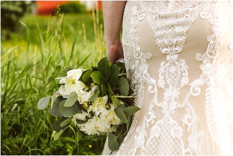 Snohomish & seattle wedding photographer | gsquared weddings photography a person in a detailed lace wedding dress stands in tall grass at marionfield farm elopement holding a bouquet of white flowers and greenery by their side | wedding photo by gsquared weddings