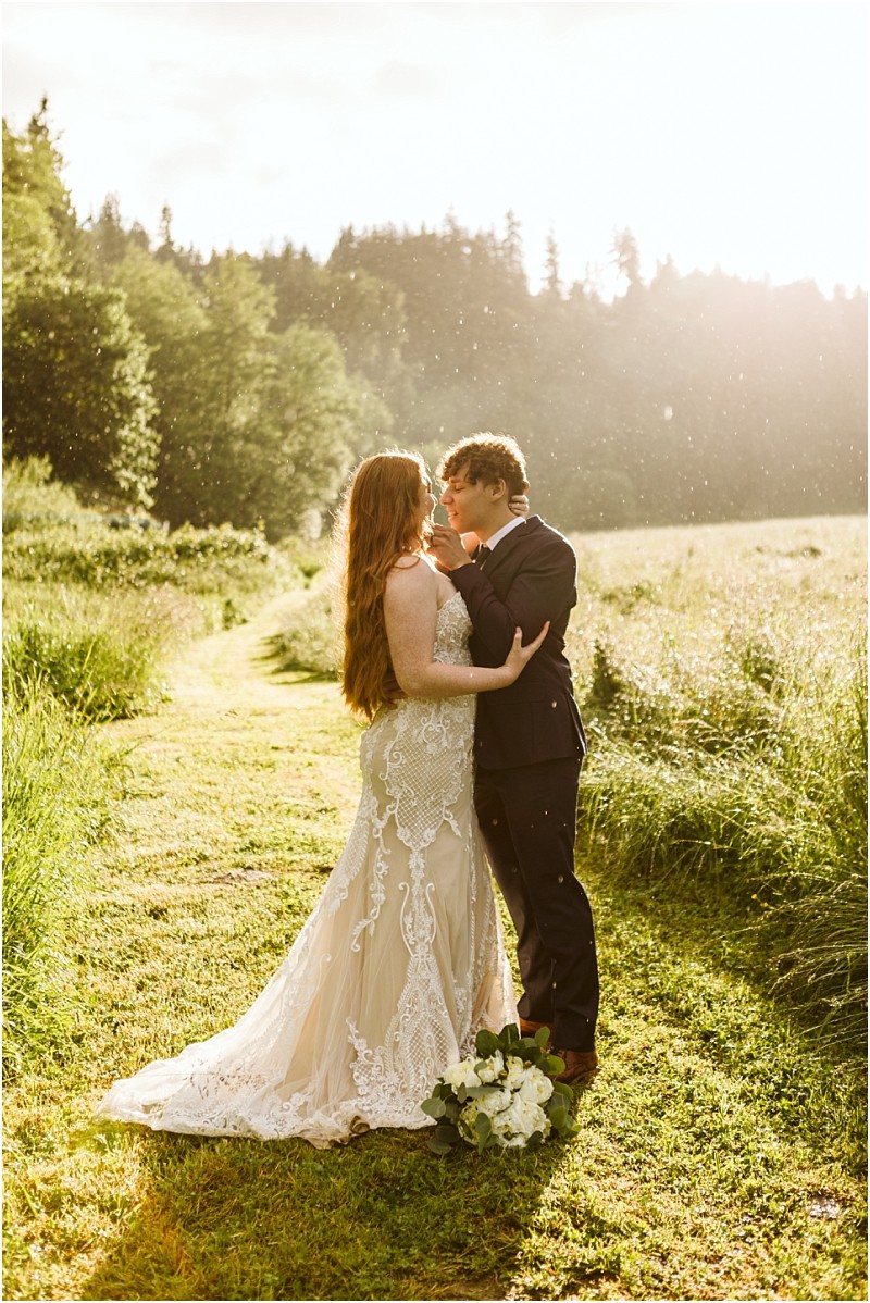 Snohomish & seattle wedding photographer | gsquared weddings photography a bride and groom stand on a grassy path at marionfield farm elopement gazing at each other lovingly The bride wears a lace dress and holds a bouquet while the groom is in a suit Soft sunlight and trees frame their moment | wedding photo by gsquared weddings