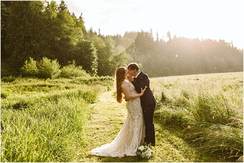 Snohomish & seattle wedding photographer | gsquared weddings photography a bride and groom embrace on a sunlit grassy path at marionfield farm surrounded by lush greenery with a wedding bouquet at their feet and warm sunlight streaming through the treesa perfect elopement moment | wedding photo by gsquared weddings