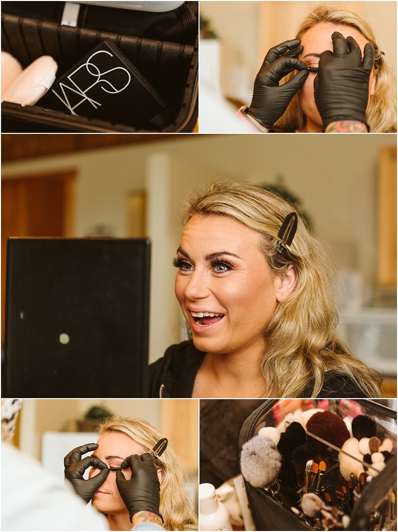 Snohomish & seattle wedding photographer | gsquared weddings photography a woman with blonde hair is getting her makeup done before her methow elopement She smiles at a mirror while a makeup artist applies eye makeup with gloved hands surrounded by makeup products and brushes | wedding photo by gsquared weddings