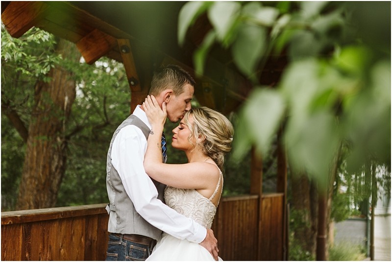Snohomish & seattle wedding photographer | gsquared weddings photography a bride and groom embrace tenderly on a wooden bridge surrounded by greenery during their methow elopement the groom kisses the brides forehead as she holds him close both dressed in wedding attire | wedding photo by gsquared weddings