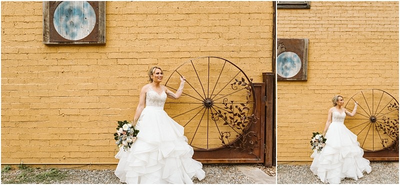 Snohomish & seattle wedding photographer | gsquared weddings photography a bride in a white gown holds a bouquet and smiles beside a large metal sculpture shaped like a wheel set against a yellow brick wall with circular artwork above her capturing the charm of a methow elopement | wedding photo by gsquared weddings