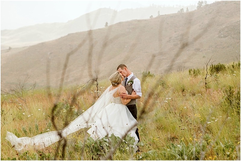 Snohomish & seattle wedding photographer | gsquared weddings photography a bride and groom embrace in a grassy meadow with rolling hills celebrating their methow elopement The brides veil flows in the wind as wildflowers surround them creating a romantic natural scene | wedding photo by gsquared weddings