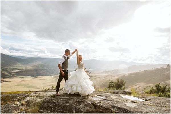 A bride and groom dance on a rocky snohomish hilltop with rolling hills and dramatic clouds in the background the brides white dress flowing as the groom twirls her under a bright sky Snohomish wedding photography