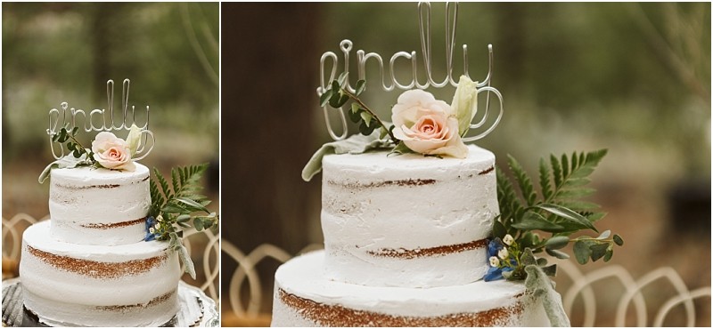 Snohomish & seattle wedding photographer | gsquared weddings photography a rustic two tiered white cake decorated with greenery a pink rose and a wire finally topperperfect for a methow elopement The cake is set outdoors with trees softly blurred in the background | wedding photo by gsquared weddings