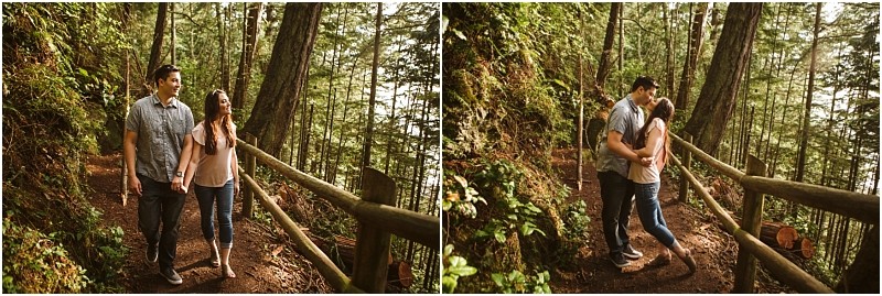 Snohomish & seattle wedding photographer | gsquared weddings photography a couple walks hand in hand along a forest trail lined with wooden railings during their deception pass engagement session in june 2020 then stops to share a kiss surrounded by tall trees and greenery | wedding photo by gsquared weddings