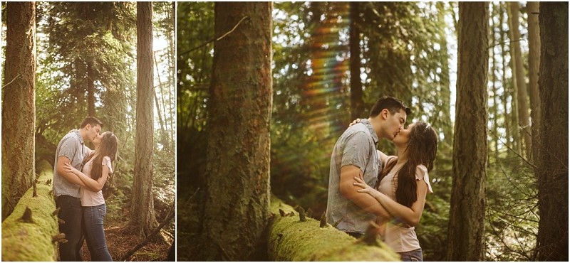 Snohomish & seattle wedding photographer | gsquared weddings photography a couple stands in a forest during their deception pass engagement session embracing and kissing near moss covered trees as sunlight filters through the branches casting a warm golden glow and a faint rainbow lens flare June 2020 | wedding photo by gsquared weddings